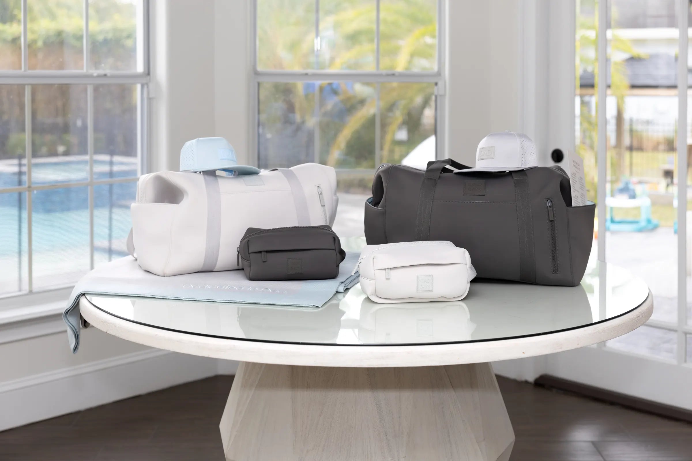 Collection of bags on a glass table with a pool and outdoor furniture in the background
